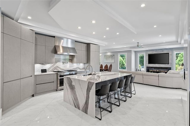 kitchen featuring marble finish floor, gray cabinetry, modern cabinets, high end range, and wall chimney exhaust hood