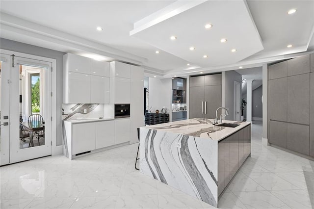 kitchen with a raised ceiling, a sink, marble finish floor, and modern cabinets