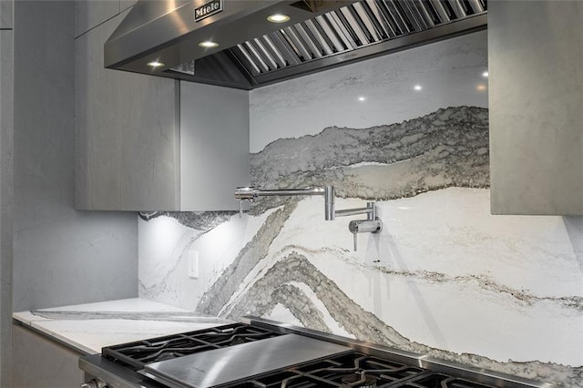 kitchen with tasteful backsplash, gas range oven, light stone counters, and extractor fan