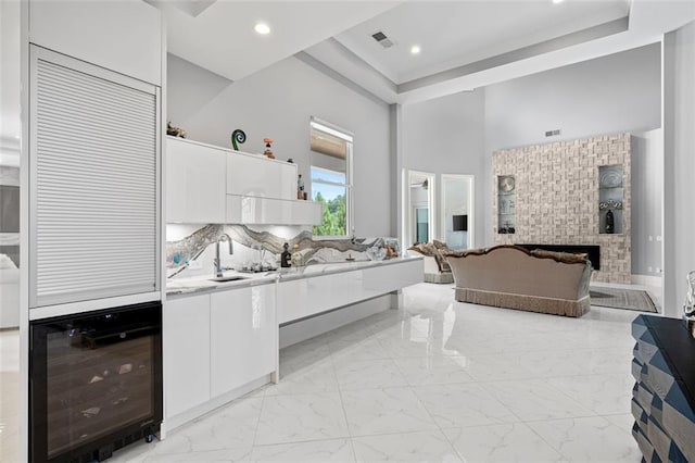 bedroom featuring wine cooler, marble finish floor, a fireplace, a raised ceiling, and a sink