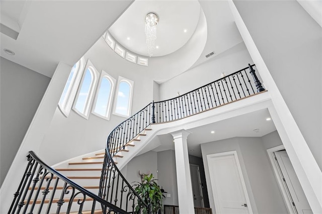 staircase with visible vents, an inviting chandelier, a high ceiling, ornate columns, and recessed lighting