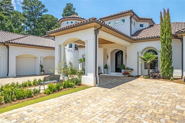 mediterranean / spanish home with a garage, driveway, a tiled roof, and stucco siding