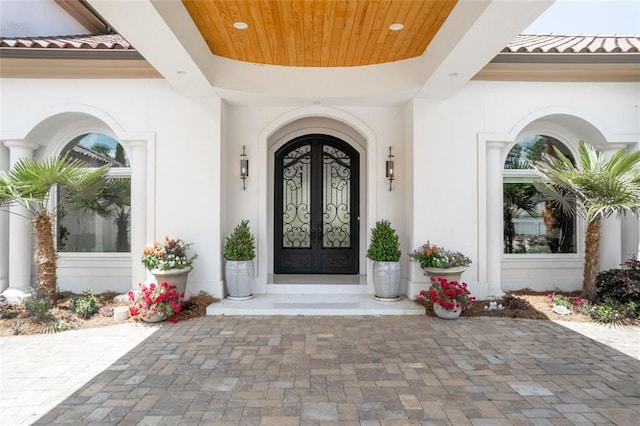 property entrance featuring a tiled roof, french doors, and stucco siding