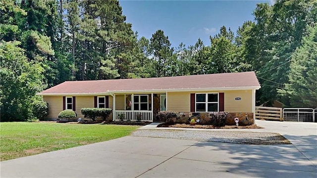 ranch-style house featuring covered porch, fence, stone siding, driveway, and a front yard