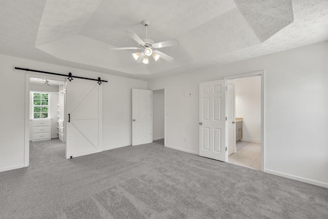 895 Roxfield Ct, Buford, GA 30518 - unfurnished bedroom with a barn door, carpet floors, a textured ceiling, baseboards, and a raised ceiling