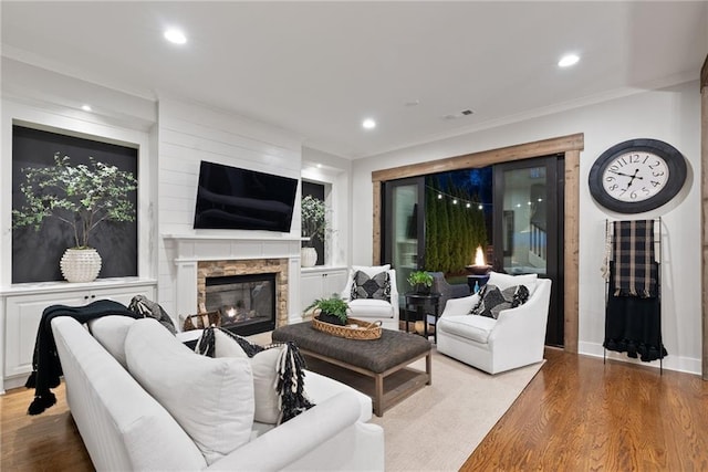 living room featuring a fireplace, crown molding, wood finished floors, and visible vents