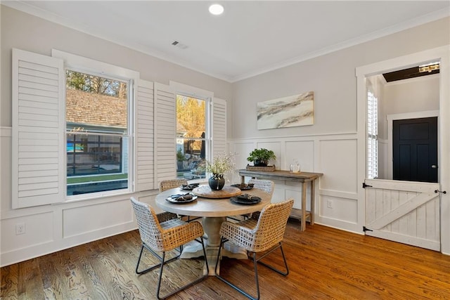 dining room featuring wood finished floors, a wainscoted wall, visible vents, crown molding, and a decorative wall