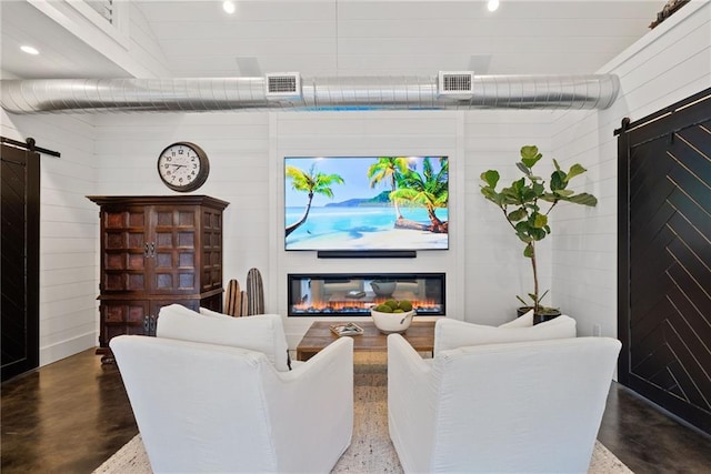 living room with a glass covered fireplace, a barn door, finished concrete flooring, and visible vents