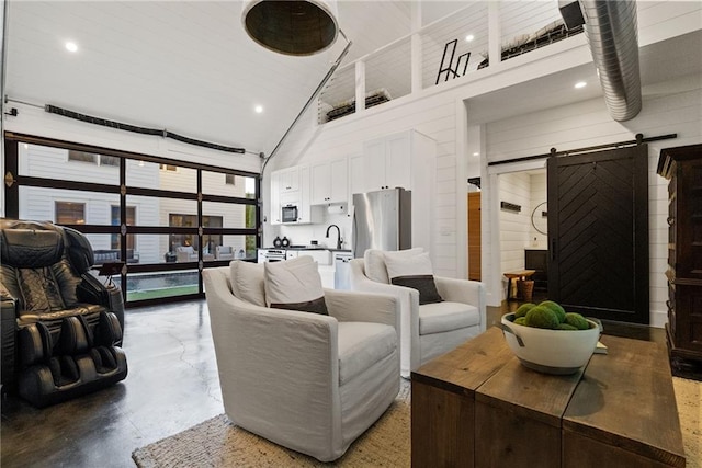 living area with high vaulted ceiling, concrete flooring, and a barn door