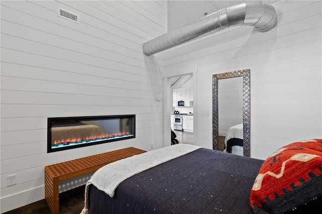 bedroom featuring a glass covered fireplace, wood walls, and visible vents