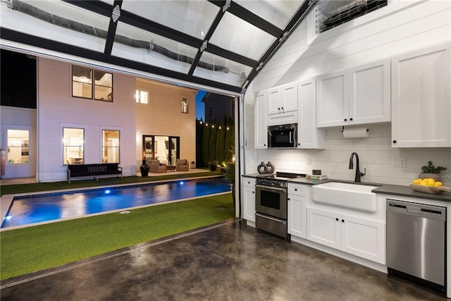 kitchen featuring high vaulted ceiling, a sink, dark countertops, stainless steel appliances, and concrete floors