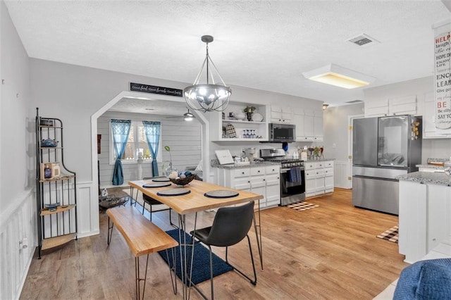 dining area featuring light wood-style floors, arched walkways, visible vents, and a textured ceiling