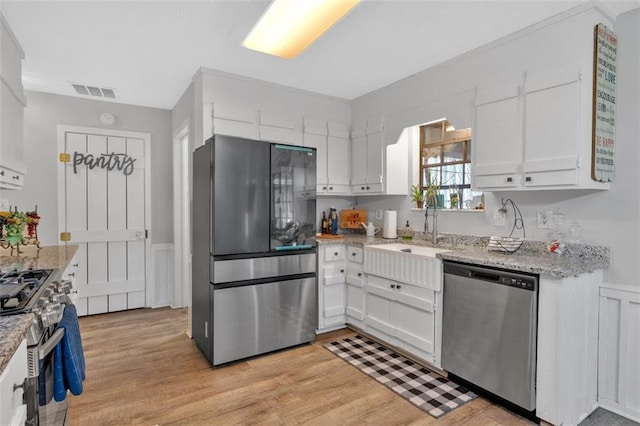 kitchen featuring light wood finished floors, visible vents, appliances with stainless steel finishes, white cabinetry, and a sink