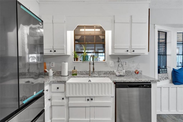 kitchen featuring dishwasher, freestanding refrigerator, and white cabinetry