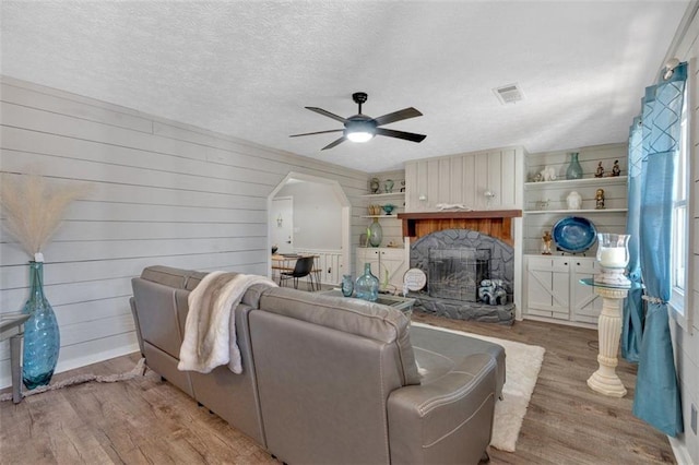 living room featuring visible vents, arched walkways, a ceiling fan, a textured ceiling, and light wood-style floors