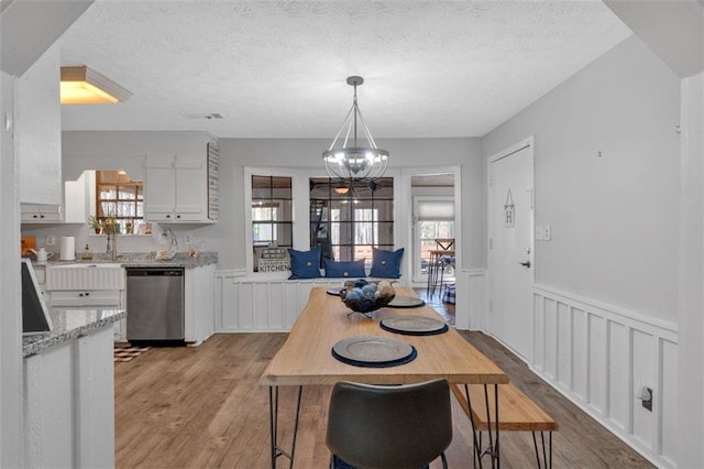 dining room featuring light wood-type flooring, wainscoting, a textured ceiling, and an inviting chandelier