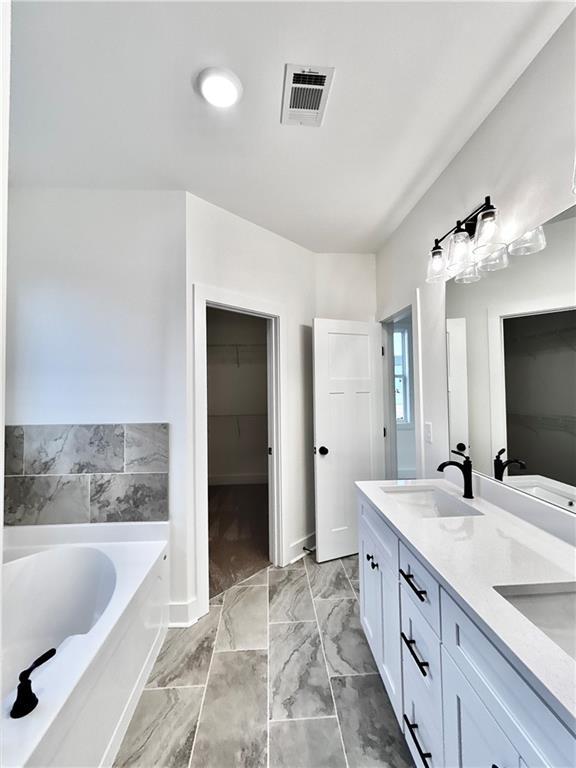 bathroom featuring a sink, visible vents, a spacious closet, a bath, and double vanity