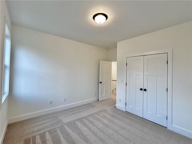 unfurnished bedroom featuring a closet, light colored carpet, and baseboards