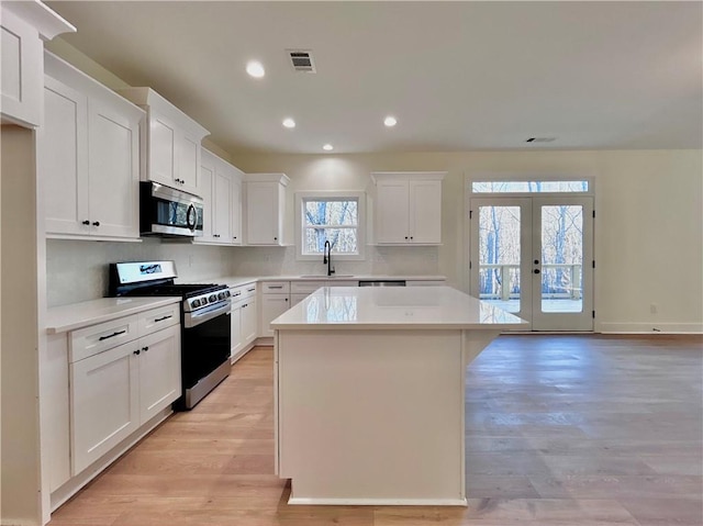 kitchen featuring stainless steel appliances, a kitchen island, a sink, visible vents, and french doors