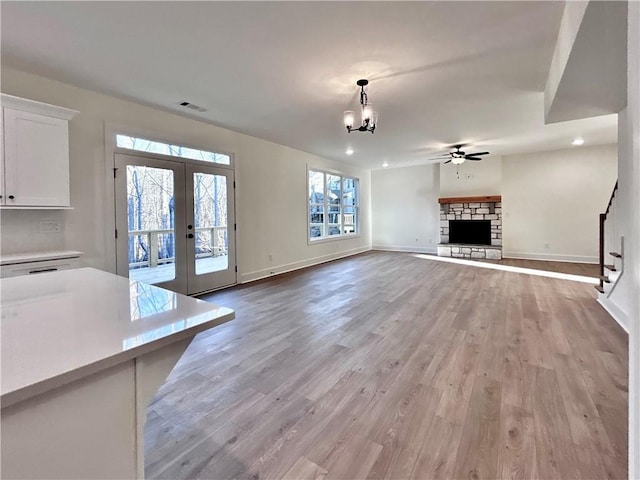 unfurnished living room with baseboards, visible vents, a fireplace with raised hearth, french doors, and light wood-type flooring