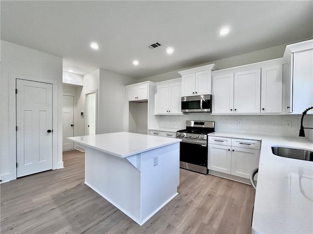 kitchen with visible vents, a kitchen island, stainless steel appliances, light wood-type flooring, and a sink