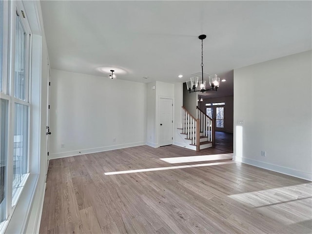 unfurnished dining area with baseboards, stairway, light wood-style flooring, and an inviting chandelier