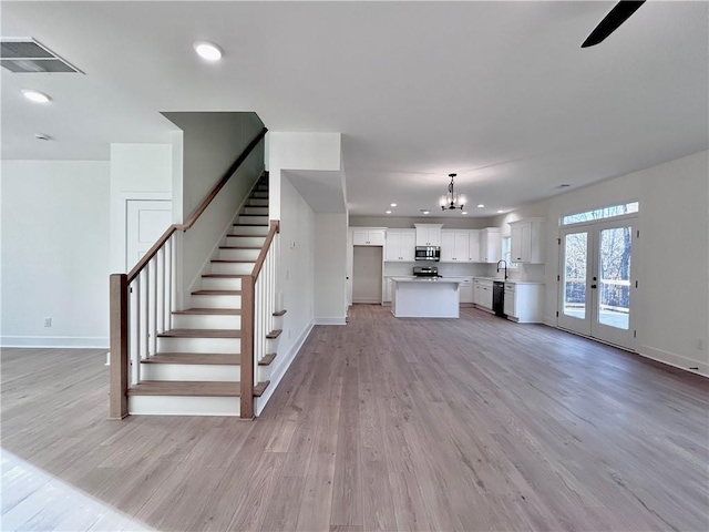 unfurnished living room with light wood-style flooring, stairway, visible vents, and baseboards