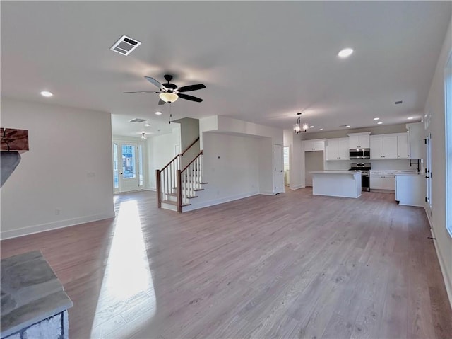 unfurnished living room featuring stairway, a sink, visible vents, and light wood-style floors