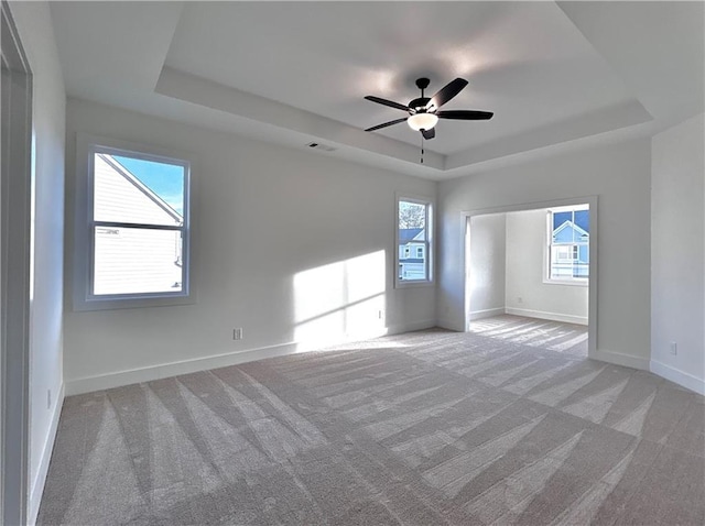 unfurnished room with baseboards, a raised ceiling, and light colored carpet