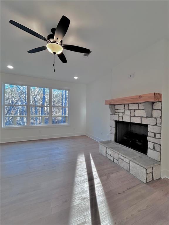 unfurnished living room featuring a stone fireplace, light wood-style flooring, recessed lighting, a ceiling fan, and baseboards