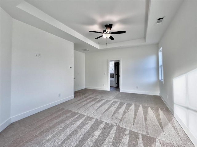 spare room featuring carpet floors, a raised ceiling, visible vents, a ceiling fan, and baseboards