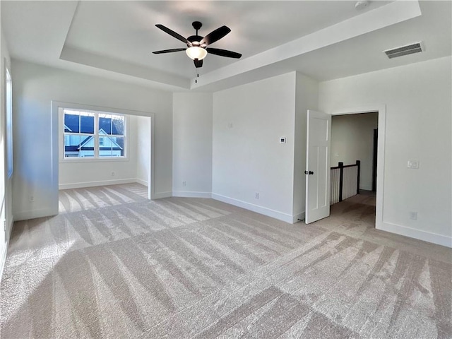 empty room with light carpet, baseboards, visible vents, and a raised ceiling