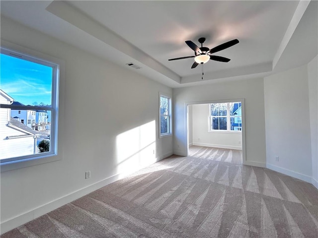 empty room featuring light carpet, visible vents, baseboards, a raised ceiling, and ceiling fan