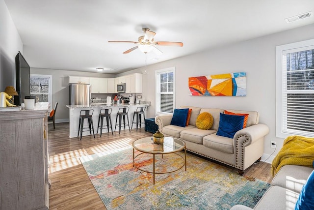 living room with light wood finished floors, baseboards, visible vents, and a ceiling fan