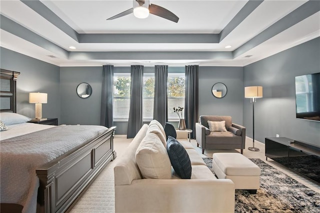 bedroom with ceiling fan, a tray ceiling, and light colored carpet