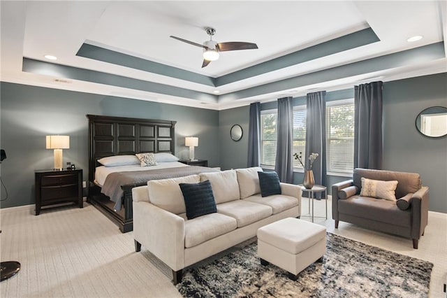 bedroom with ceiling fan, light carpet, and a tray ceiling