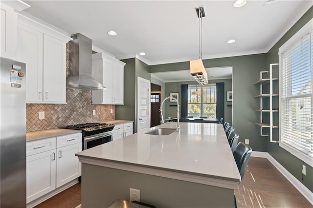 kitchen featuring white cabinetry, a kitchen island with sink, stainless steel appliances, wall chimney exhaust hood, and decorative light fixtures