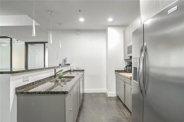 kitchen featuring baseboards, concrete flooring, dark stone countertops, appliances with stainless steel finishes, and a sink