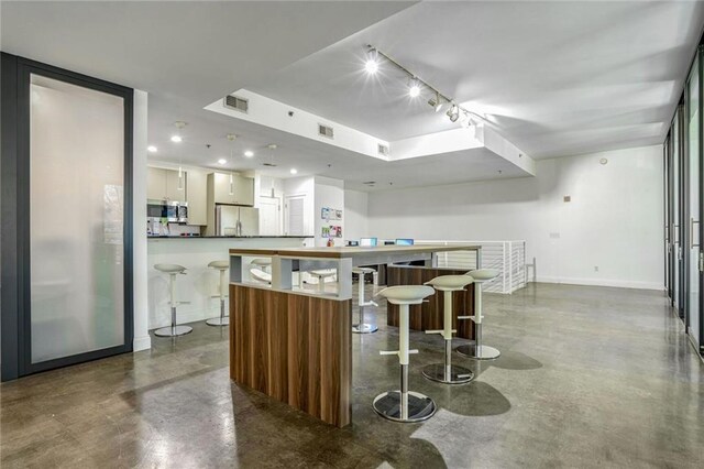kitchen featuring visible vents, baseboards, concrete floors, and stainless steel refrigerator with ice dispenser