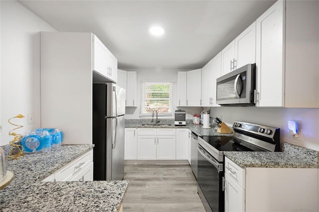 kitchen with light stone countertops, appliances with stainless steel finishes, sink, white cabinets, and light hardwood / wood-style floors