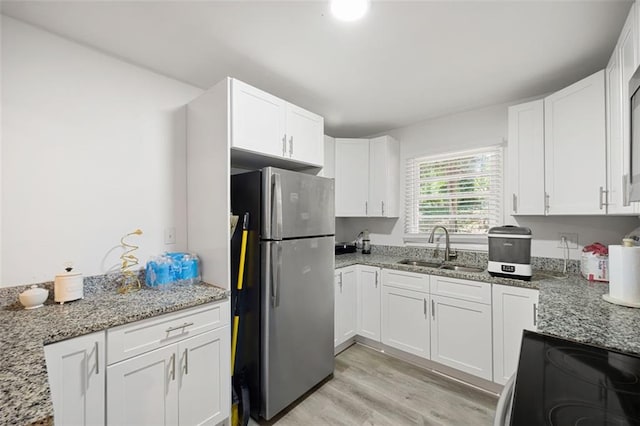 kitchen featuring light stone countertops, stainless steel fridge, sink, white cabinets, and range