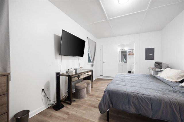 bedroom featuring light wood-type flooring, electric panel, and ensuite bathroom