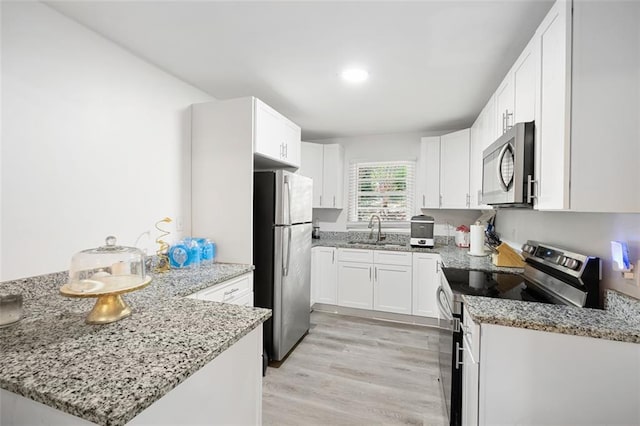 kitchen with white cabinetry, sink, stainless steel appliances, light stone counters, and kitchen peninsula