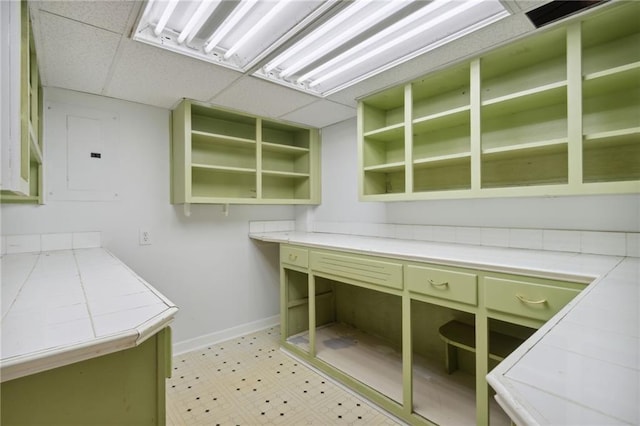 interior space featuring a paneled ceiling, green cabinetry, electric panel, and tile countertops