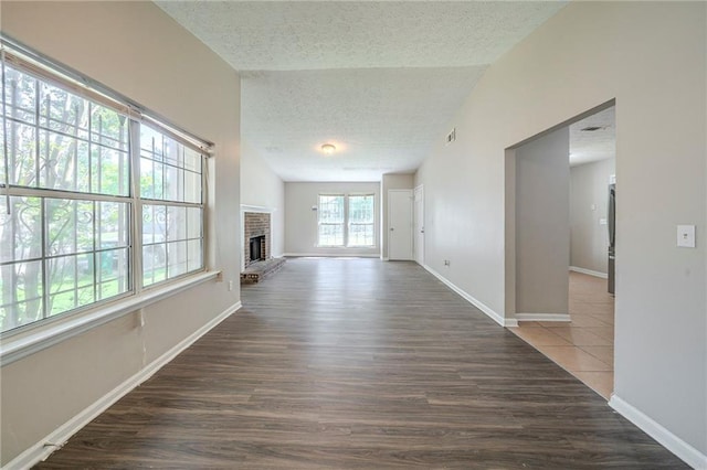 unfurnished living room with a textured ceiling, vaulted ceiling, baseboards, wood finished floors, and a fireplace