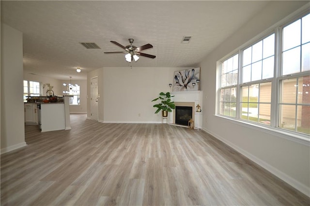 unfurnished living room featuring light hardwood / wood-style floors, a textured ceiling, and ceiling fan with notable chandelier