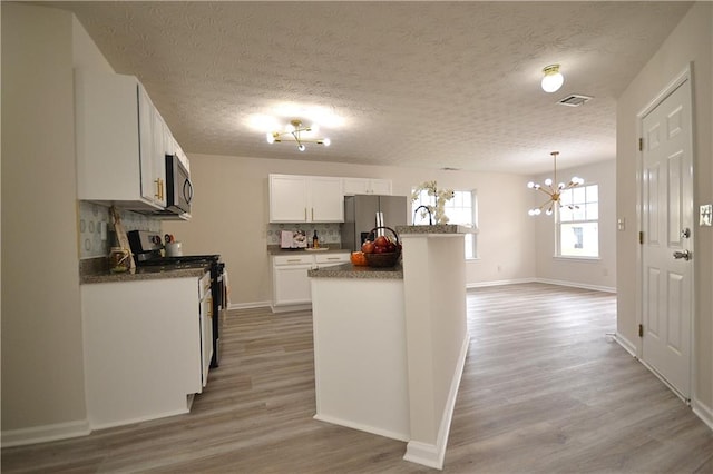 kitchen with appliances with stainless steel finishes, a textured ceiling, hanging light fixtures, hardwood / wood-style floors, and white cabinets