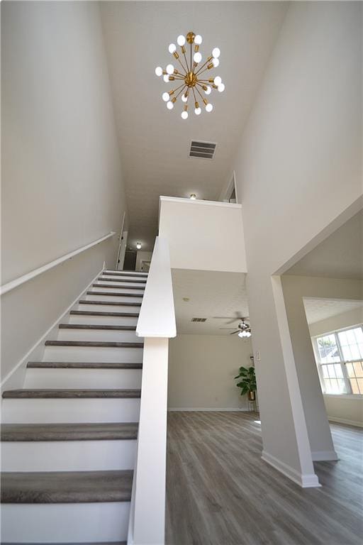 stairs featuring a towering ceiling, ceiling fan with notable chandelier, and hardwood / wood-style floors