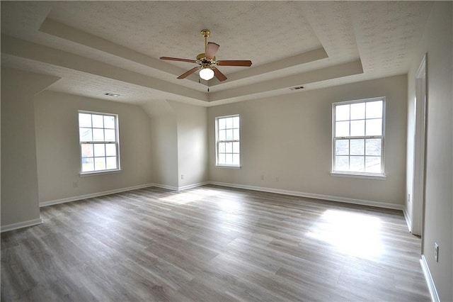 empty room with light hardwood / wood-style floors, a textured ceiling, a tray ceiling, and ceiling fan