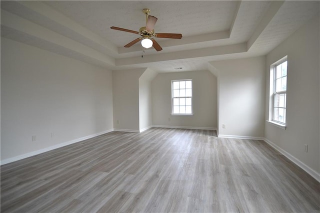 empty room with light hardwood / wood-style floors, a tray ceiling, and ceiling fan